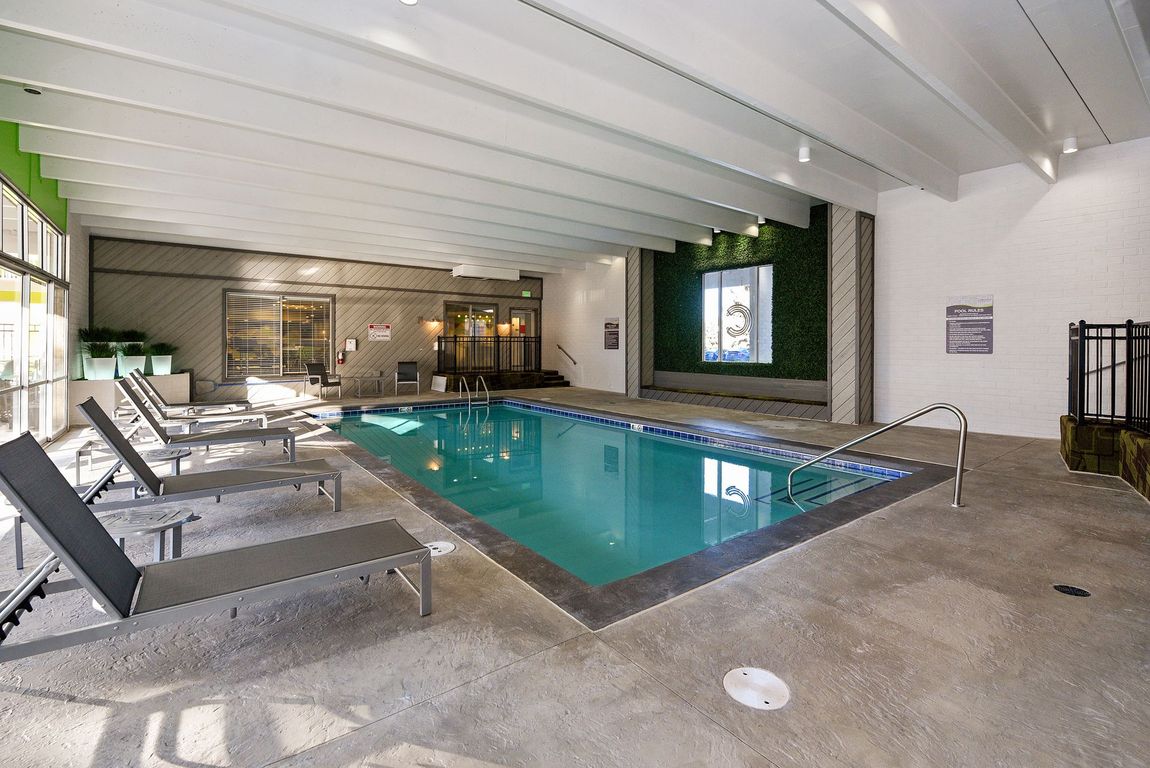 Indoor pool with lounge chairs, turquoise water, and a covered patio setting