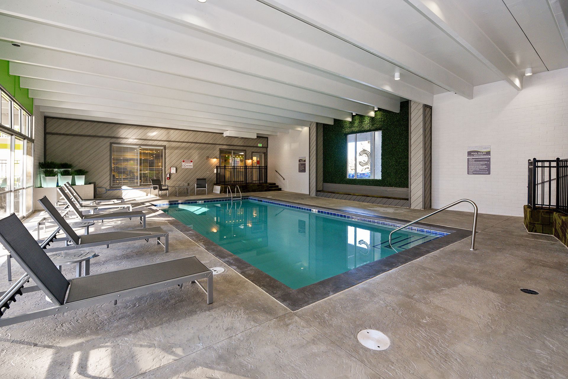 Indoor pool with lounge chairs, white ceiling beams, and a wall mural in a modern recreation area