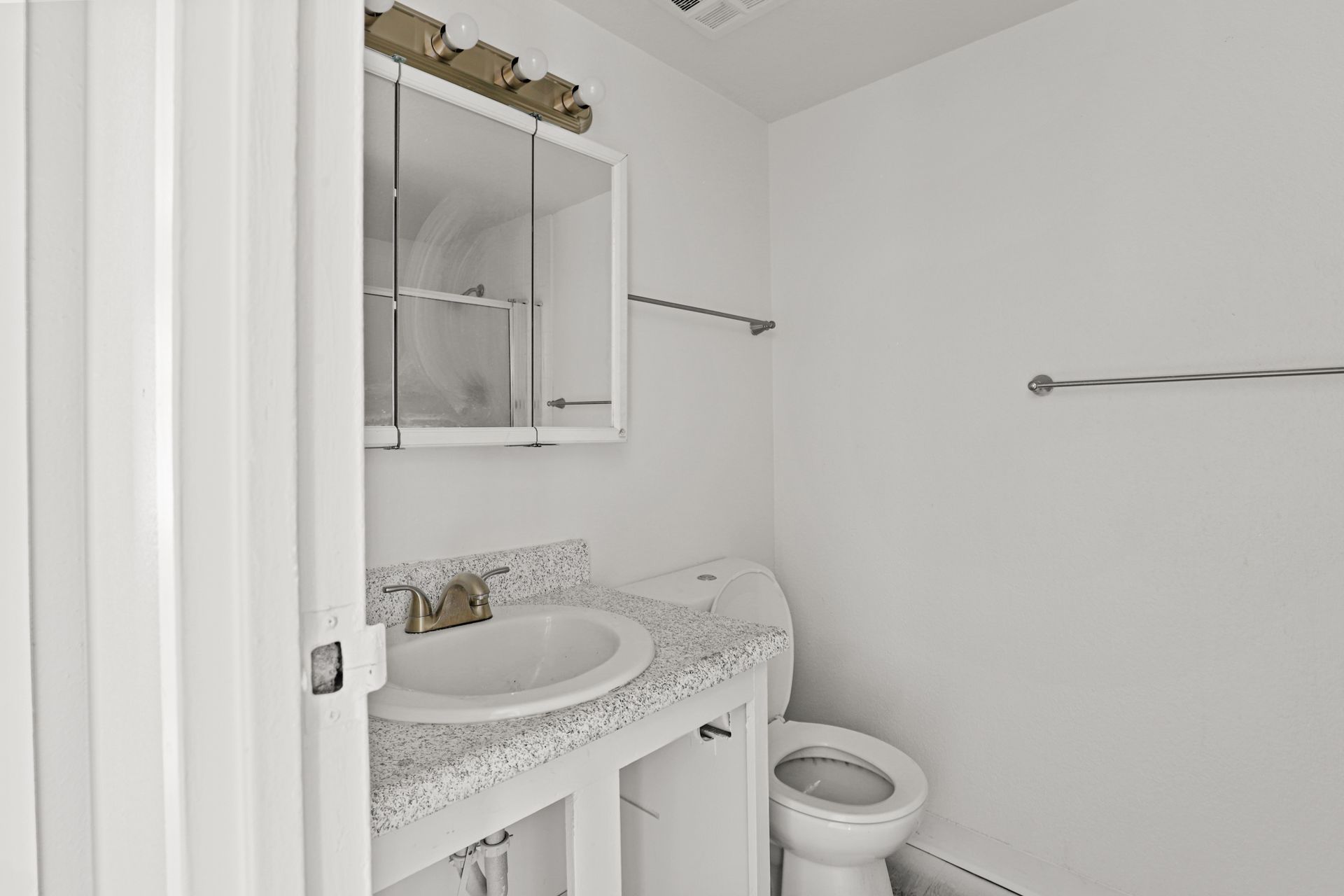 Small white bathroom with sink, mirror cabinet, towel bars, and toilet