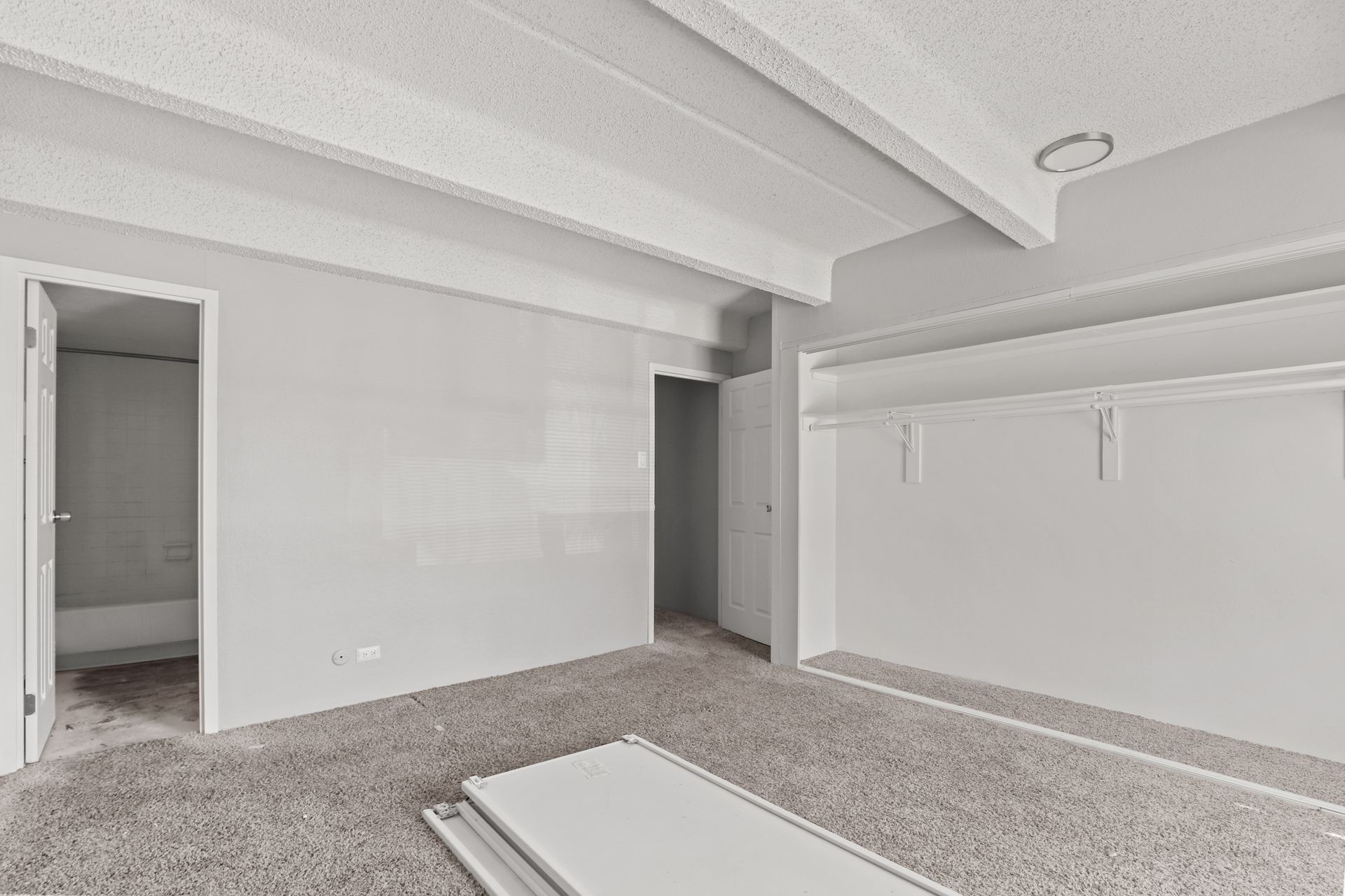Empty carpeted room with white walls, exposed ceiling beams, and two doorways