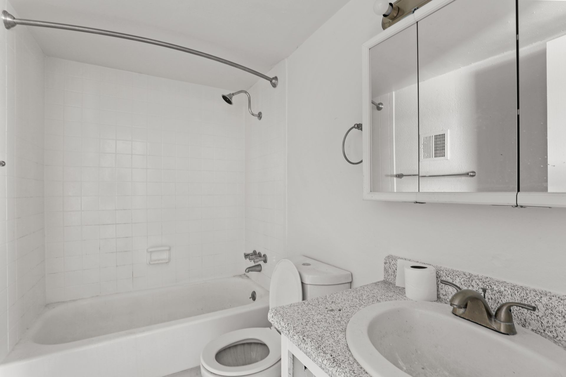 White bathroom with tub, toilet, and sink vanity, featuring a mirrored cabinet and marble countertop.