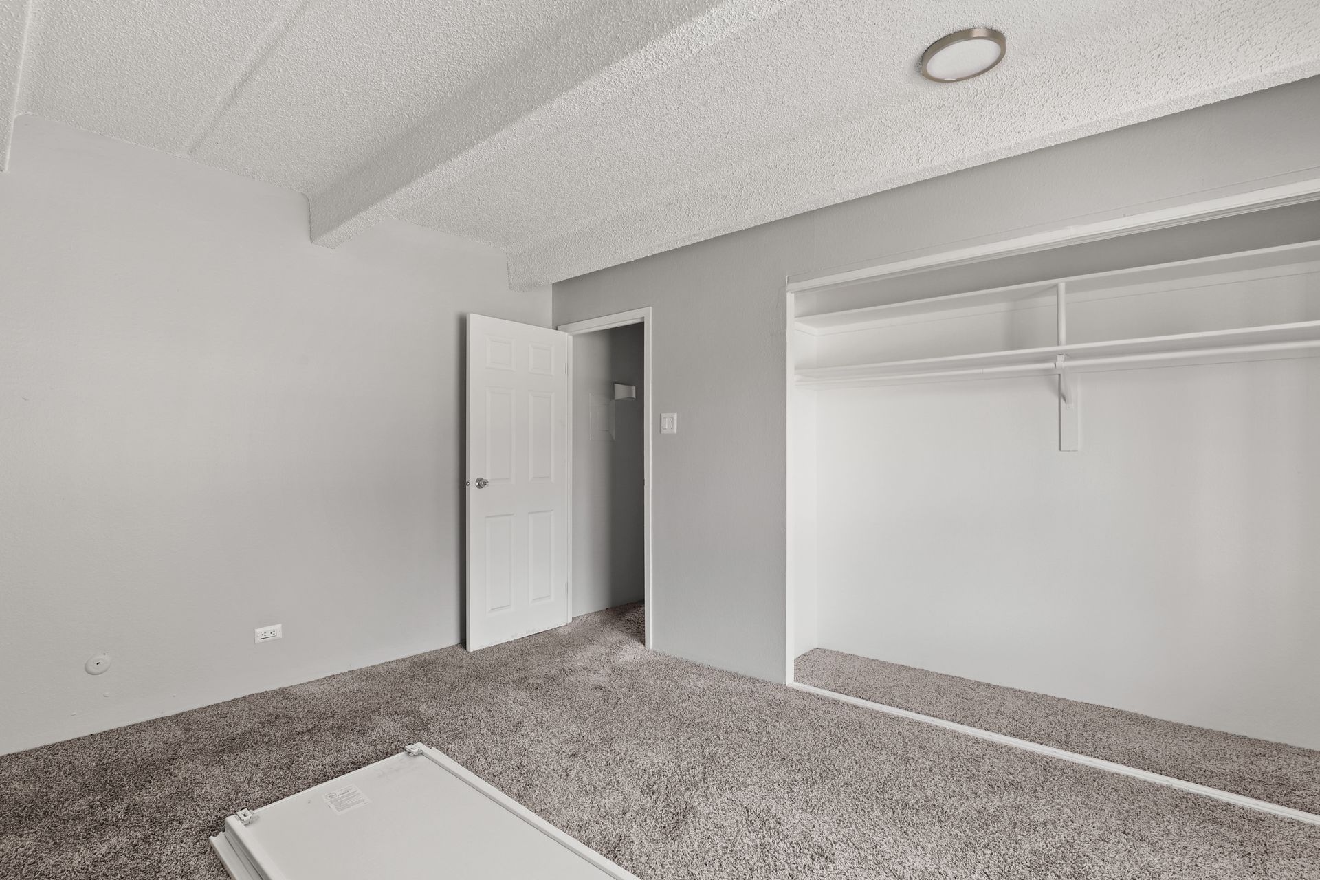 Empty gray-carpeted bedroom with open closet and white doors under a sloped ceiling.