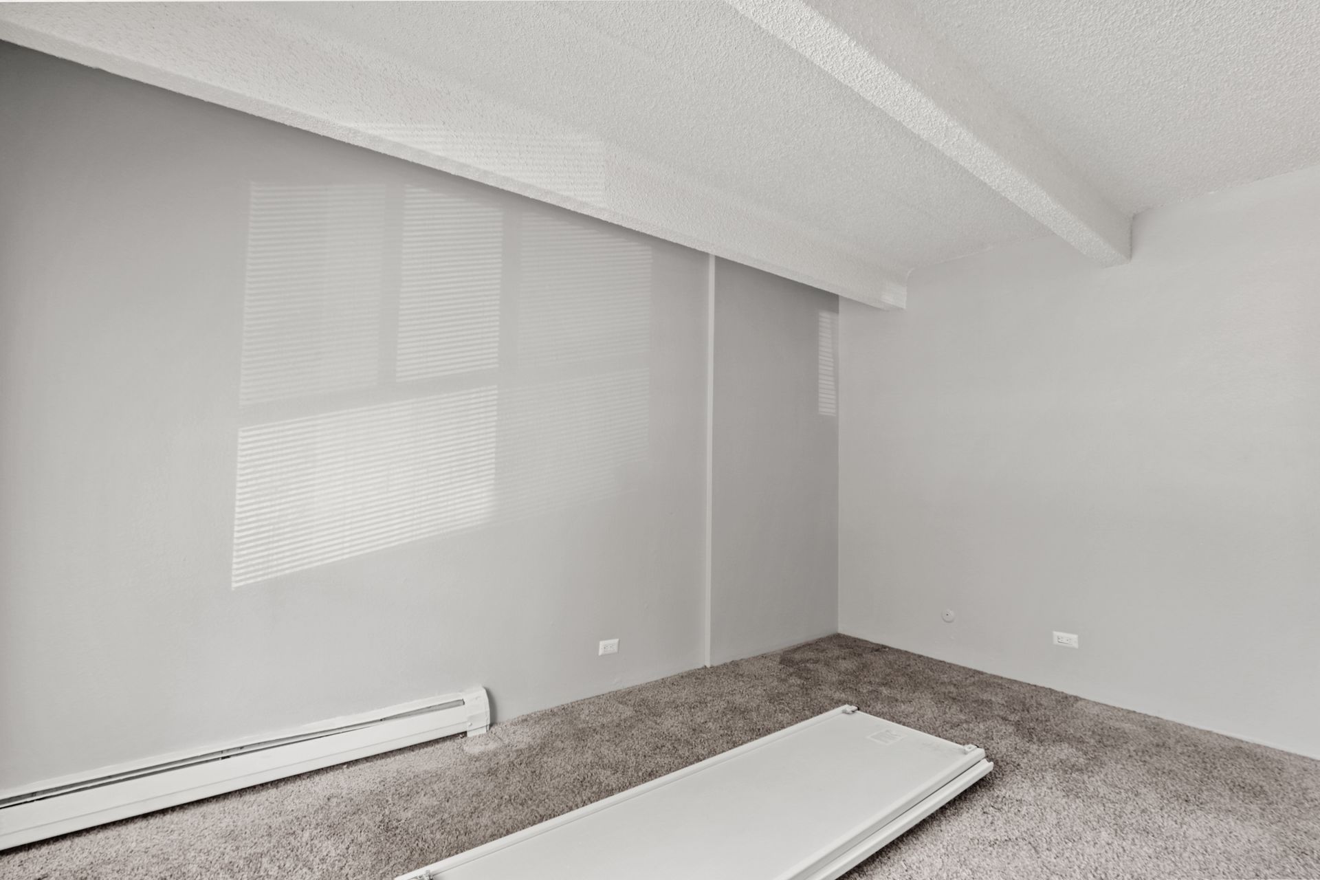 Empty white bedroom with carpet, sloped ceiling, and a mattress on the floor