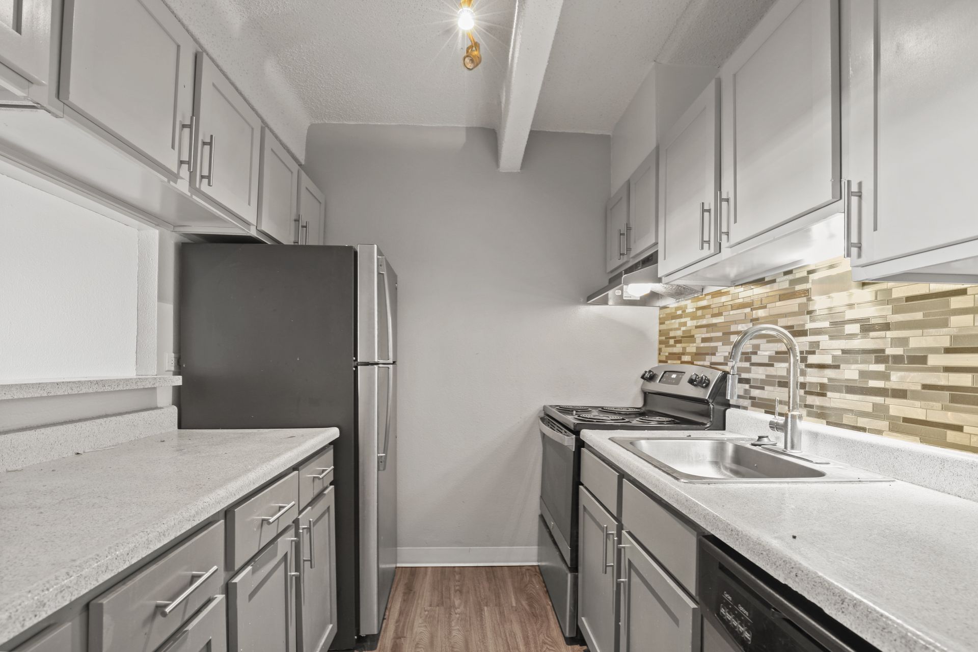 Modern galley kitchen with gray cabinets, white counters, stainless fridge, and tiled backsplash