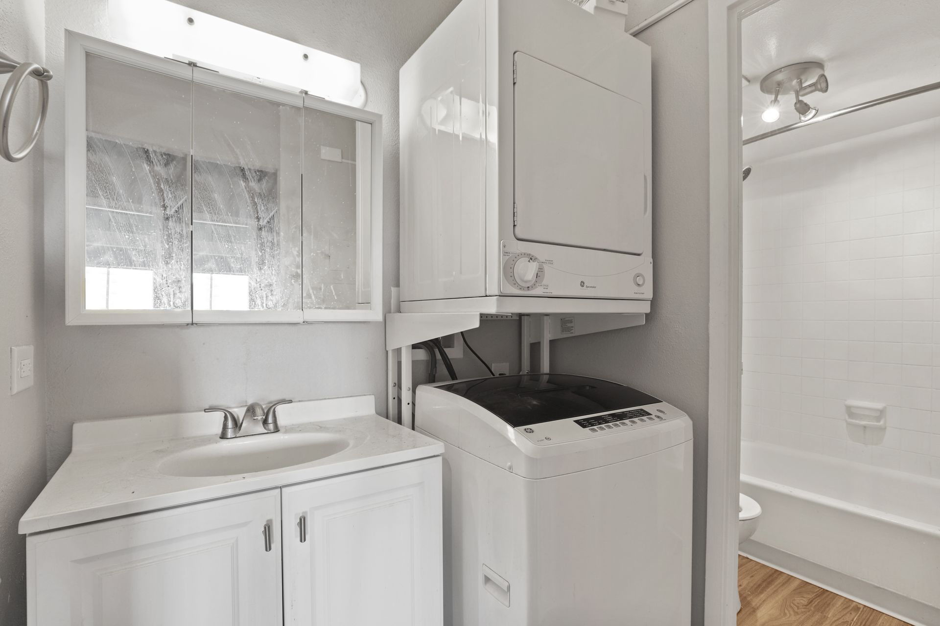Small laundry room with white washer, sink, cabinets, and a shower stall visible beside it.