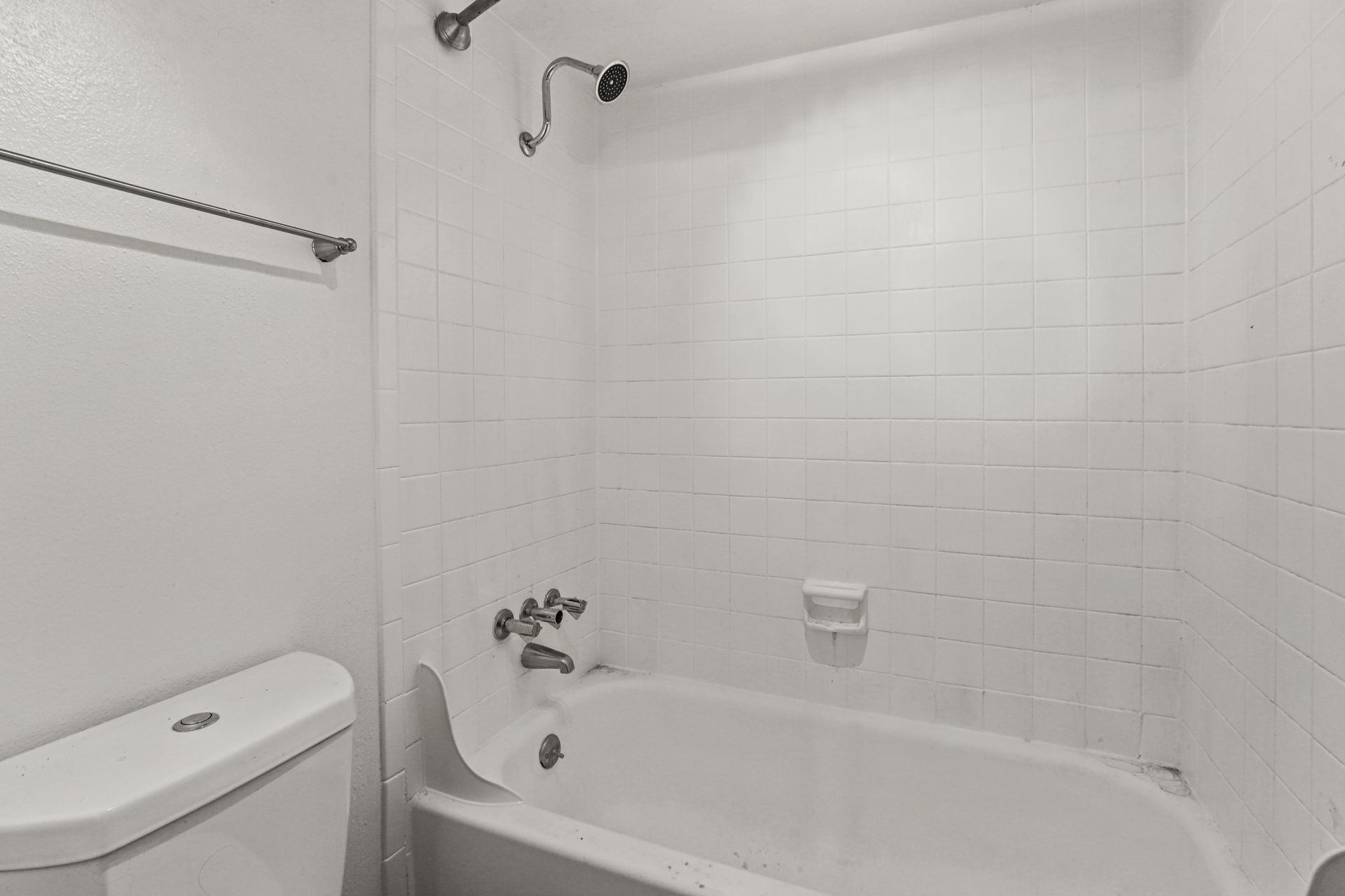 White bathroom with a bathtub, toilet, and shower curtain rod.