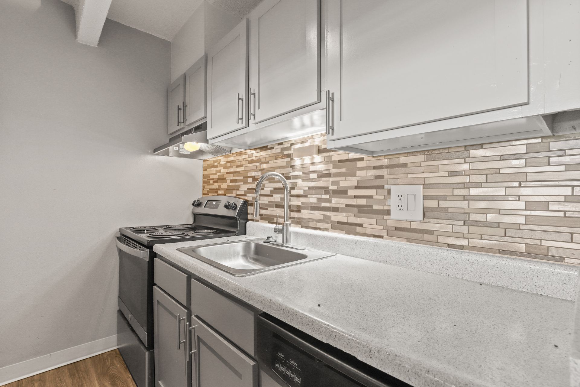 Modern kitchen with gray cabinets, white countertops, stainless stove, and a stone tile backsplash