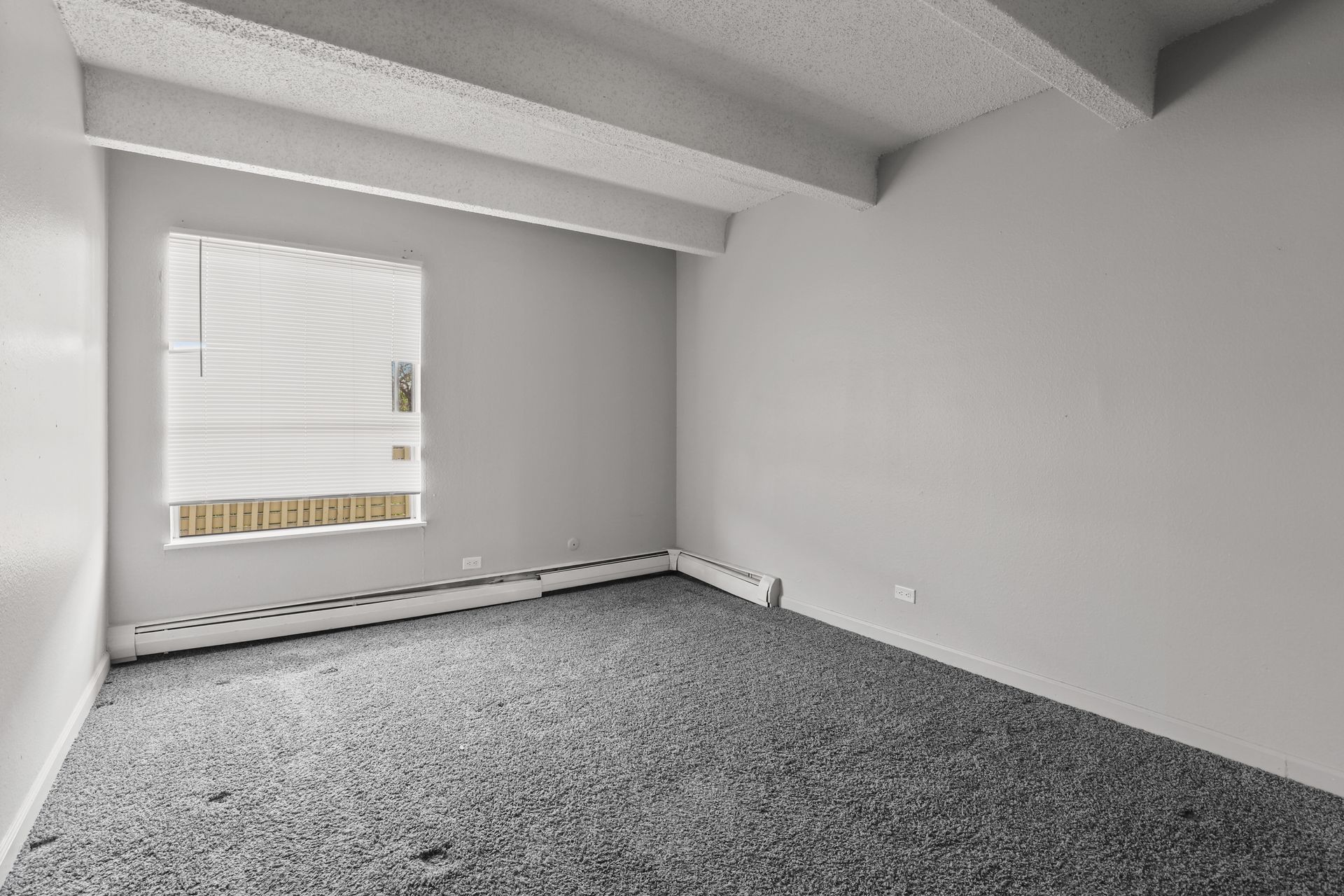 Empty gray bedroom with carpet, a window with blinds, and a sloped ceiling.