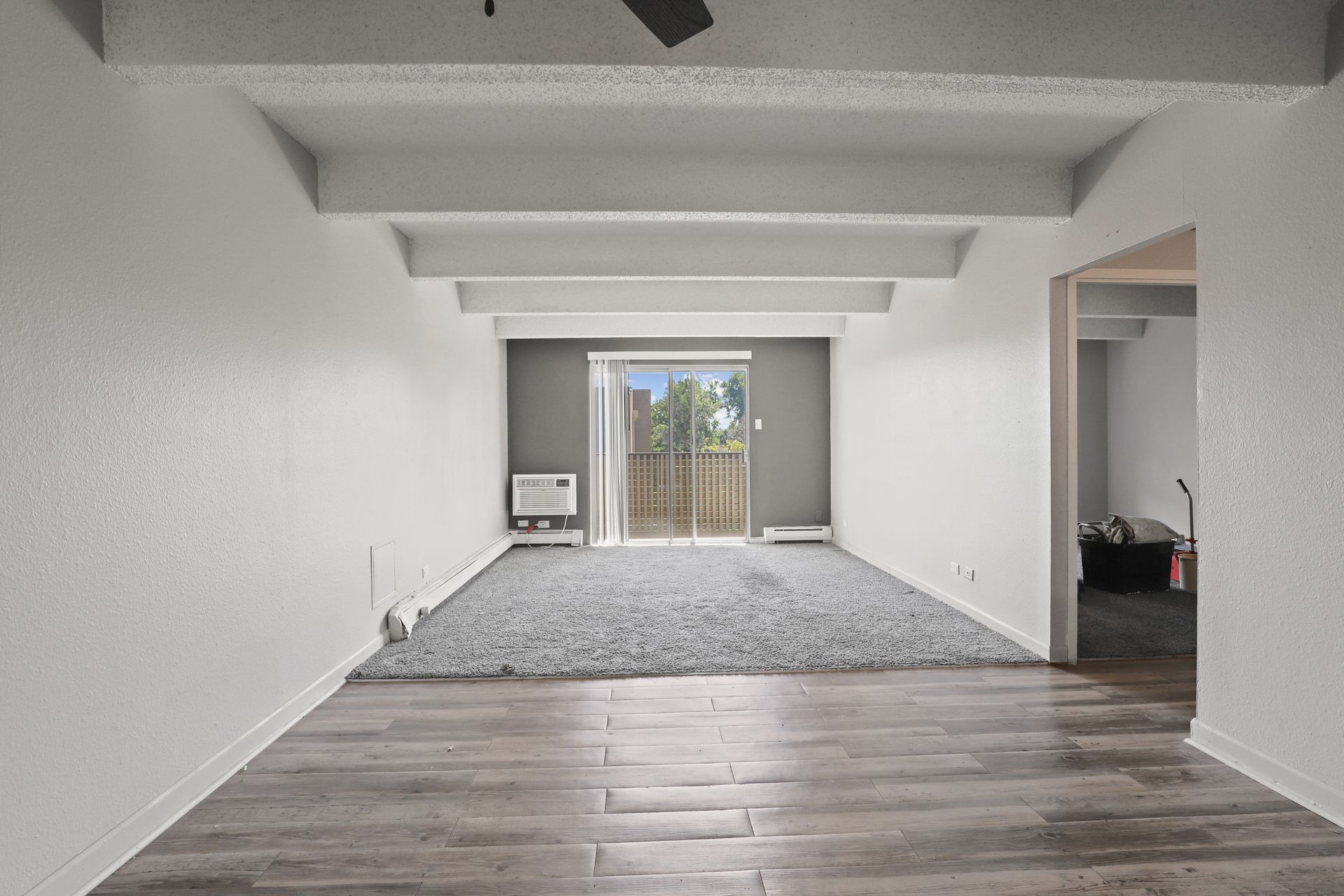 Empty living room with white walls, gray carpet, and sliding glass doors leading outside