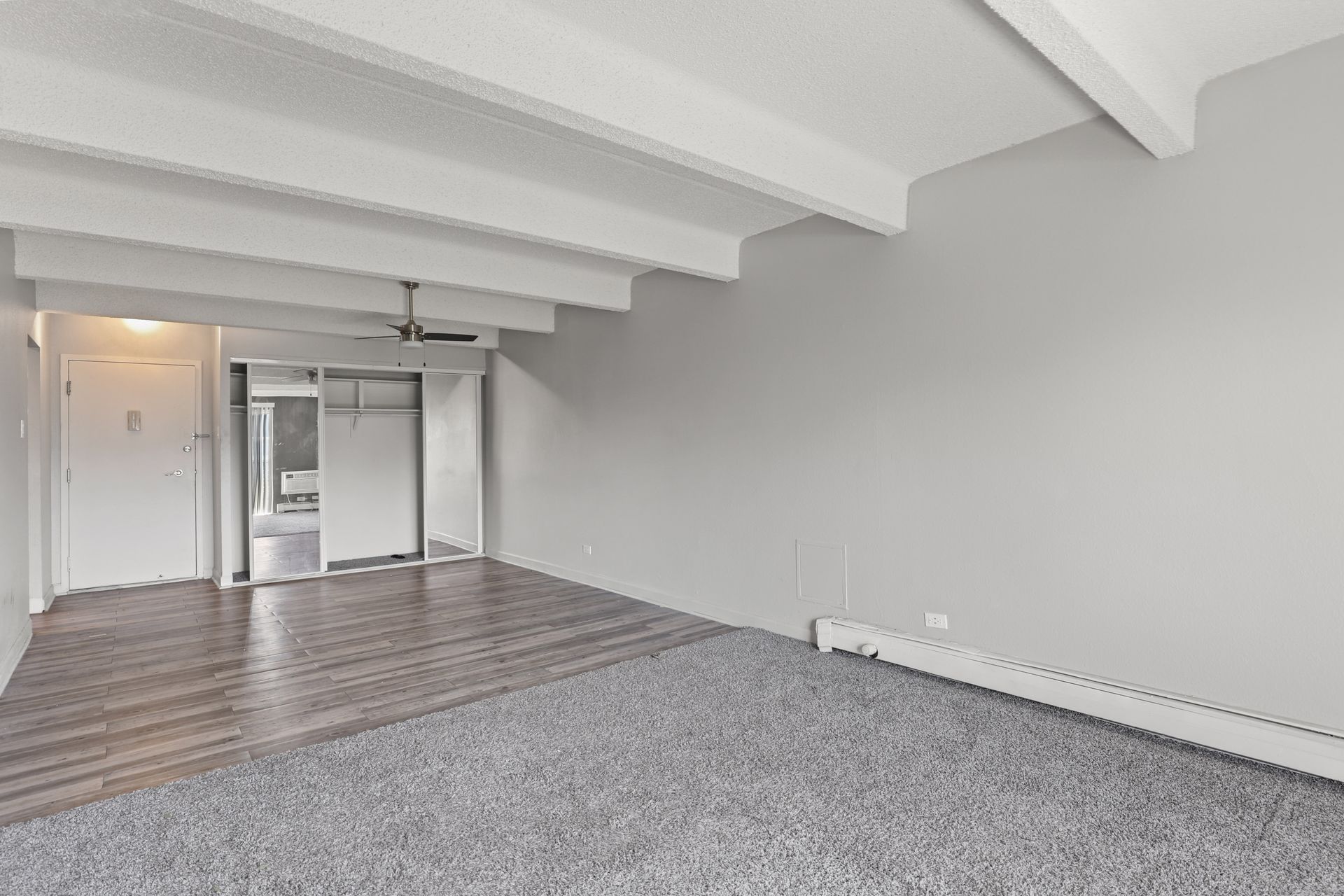 Empty carpeted room with exposed beams, gray walls, and a doorway at the far end