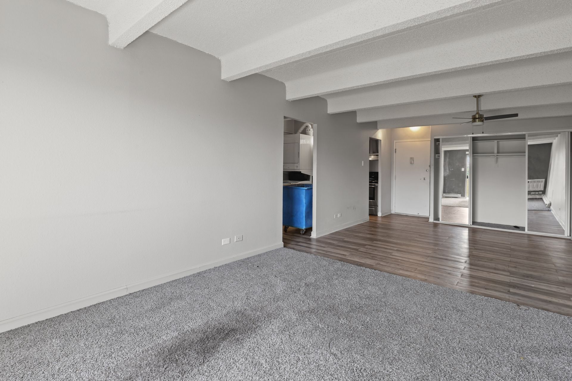Empty modern apartment living room with gray carpet, white beams, and wood flooring in back area