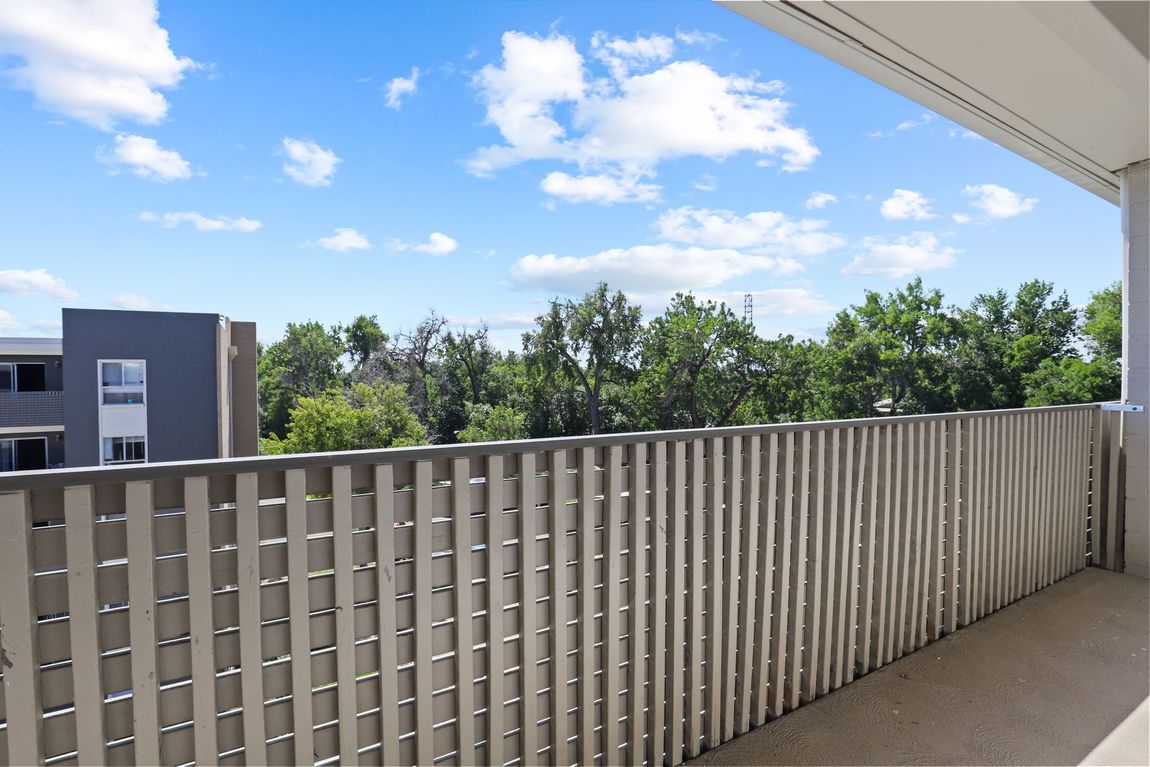 Balcony with beige railing overlooking trees and a blue sky with clouds