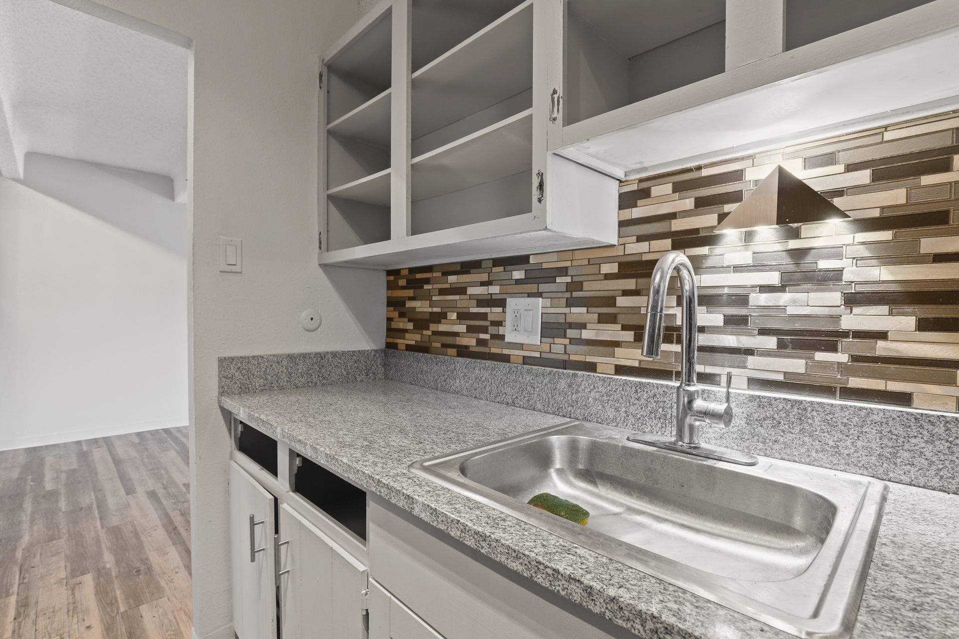 Modern kitchen with granite counter, stainless sink, open shelving, and mosaic tile backsplash