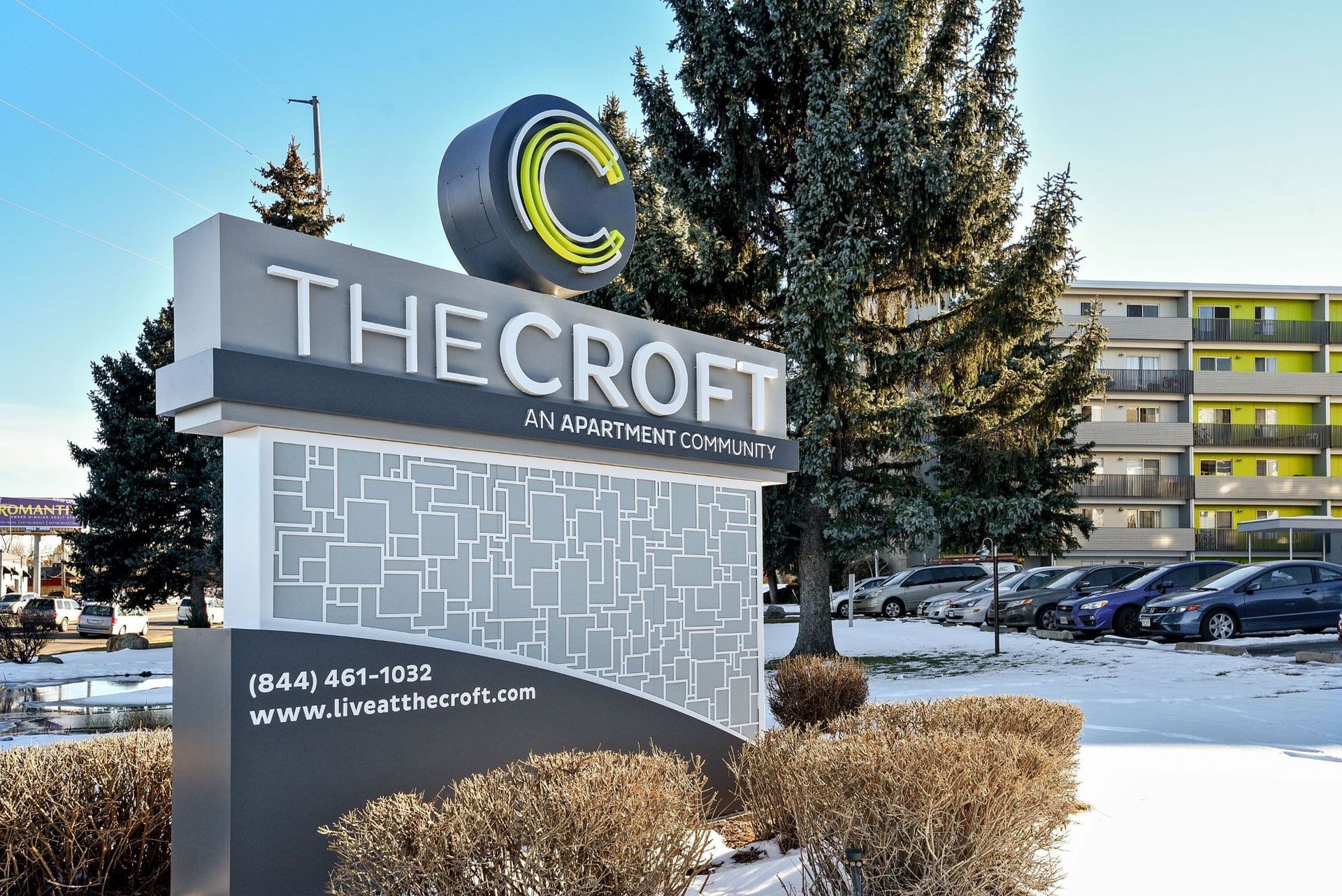 Snowy apartment complex sign reading “THE CROFT” with parked cars and tall trees at dusk