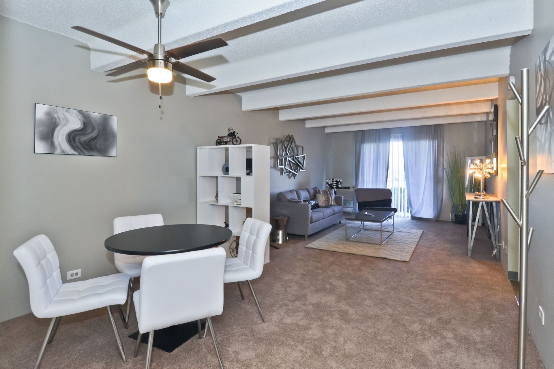 Bright open dining and living room with white chairs, gray walls, and a ceiling fan.