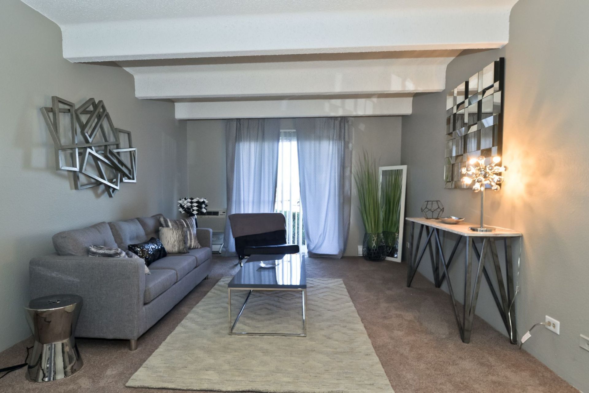 Modern living room with gray sofa, glass coffee table, TV, and sliding curtains.