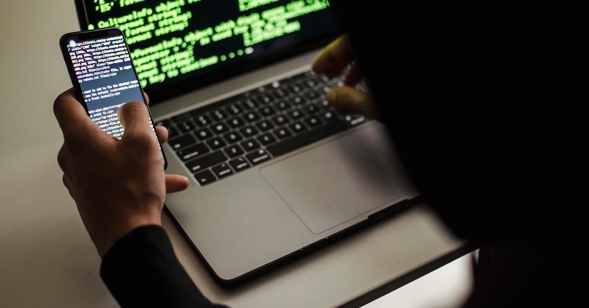 A person is holding a cell phone in front of a laptop computer.