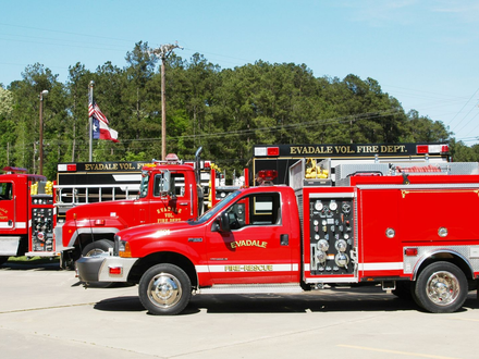 A side view of a red and blue fire engine parked on a bridge during twilight, with a car visible in the distance.