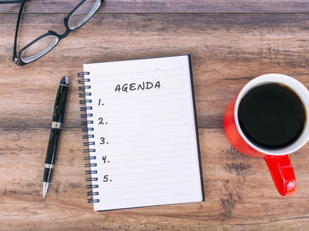 A person holds a smartphone in one hand and uses a pencil to write in a paper planner at a desk.
