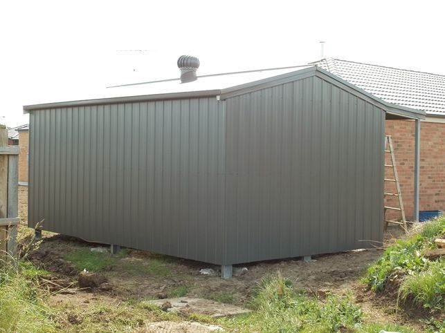 A shed is sitting in the grass next to a house.