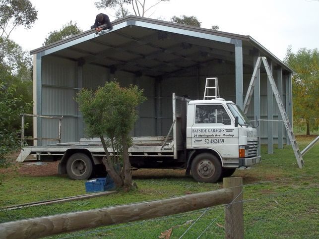 A white truck is parked in front of a building with a ladder on top of it.