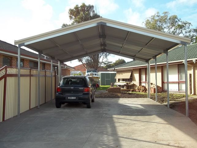 A car is parked under a carport in front of a house.