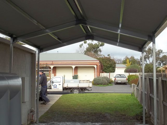 A truck is parked under a canopy in front of a house