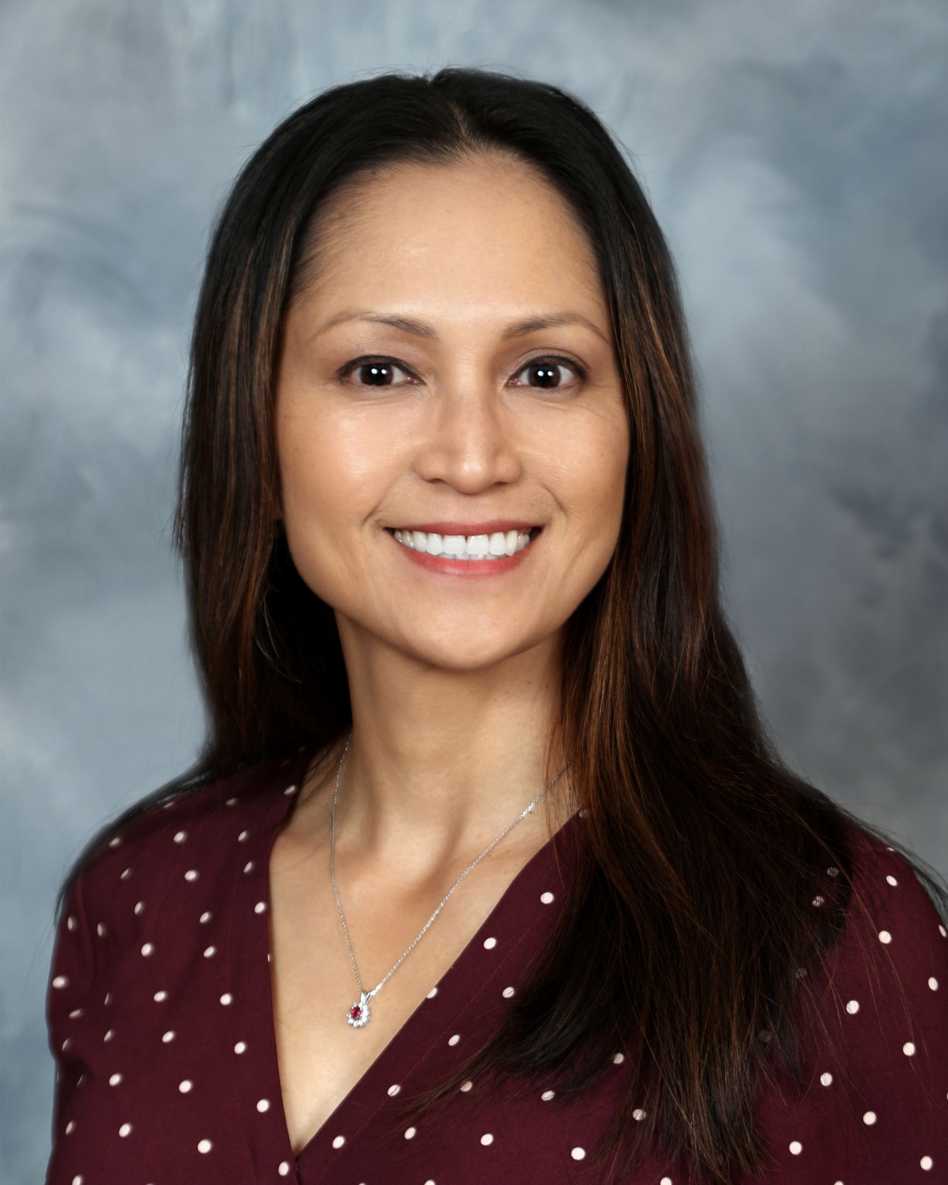Woman with brown hair in a white shirt, smiling slightly, arms crossed, in front of a gray background.