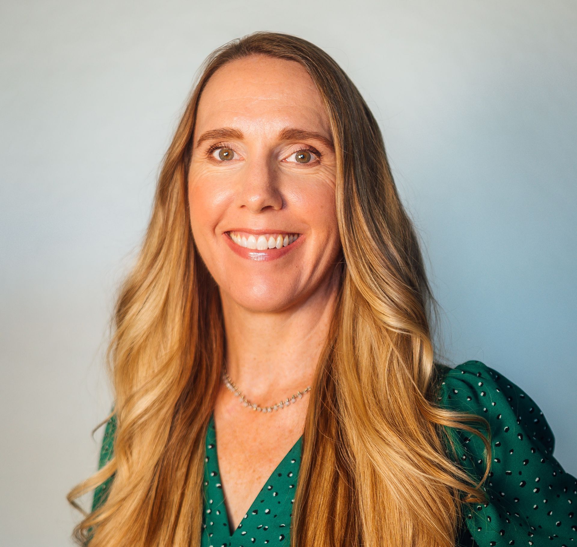 Woman with long blonde hair smiles; navy floral print top, blue and gray background.