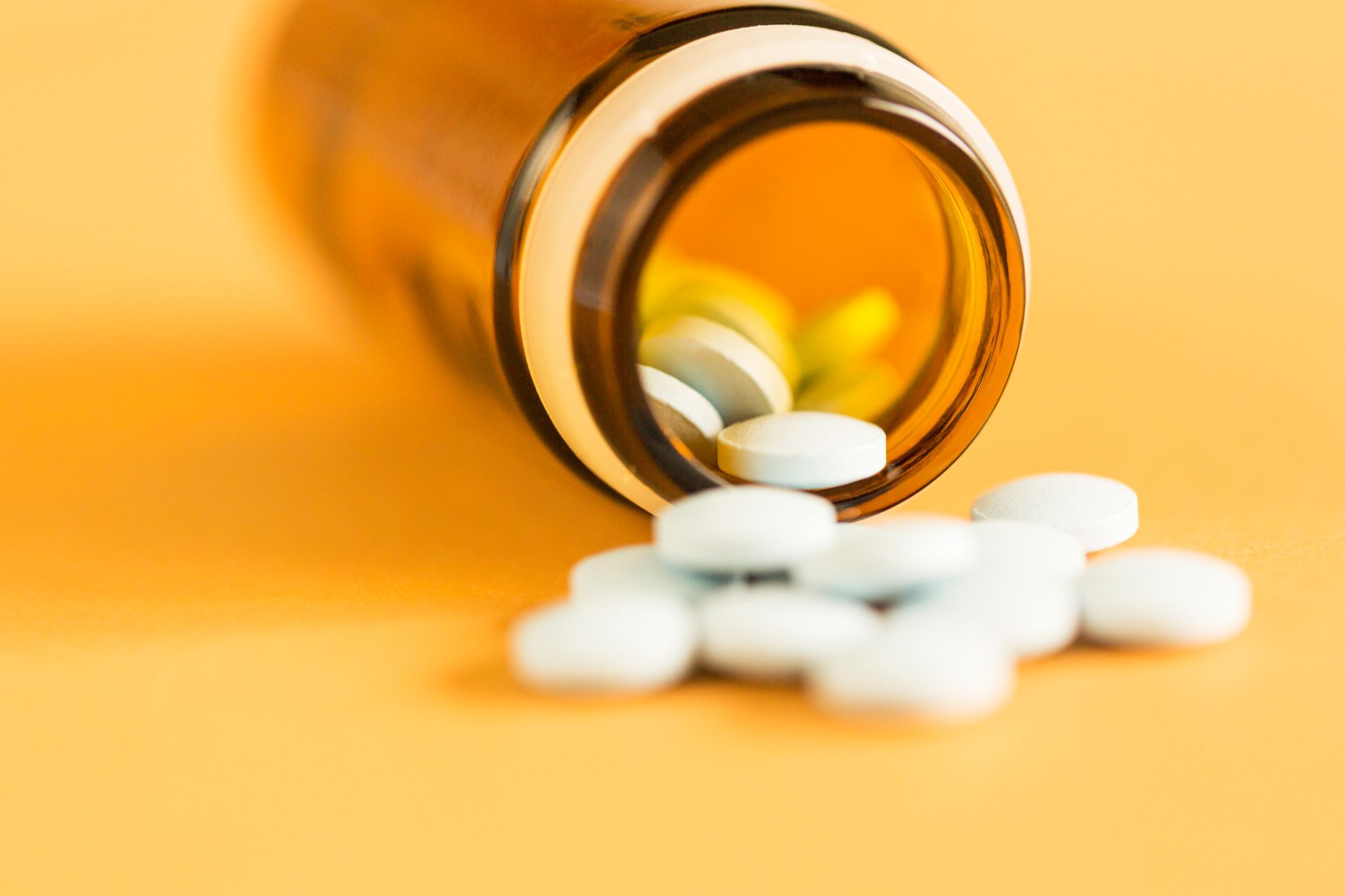 Bottle of pills spilling onto a yellow surface; some pills are visible inside the bottle.