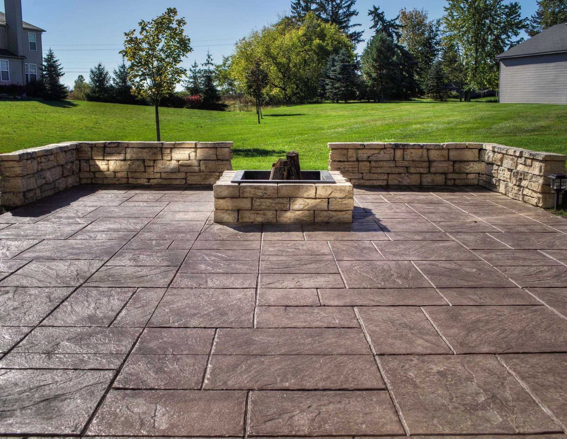 Patio with stone blocks, fire pit, and a grass yard in daylight.