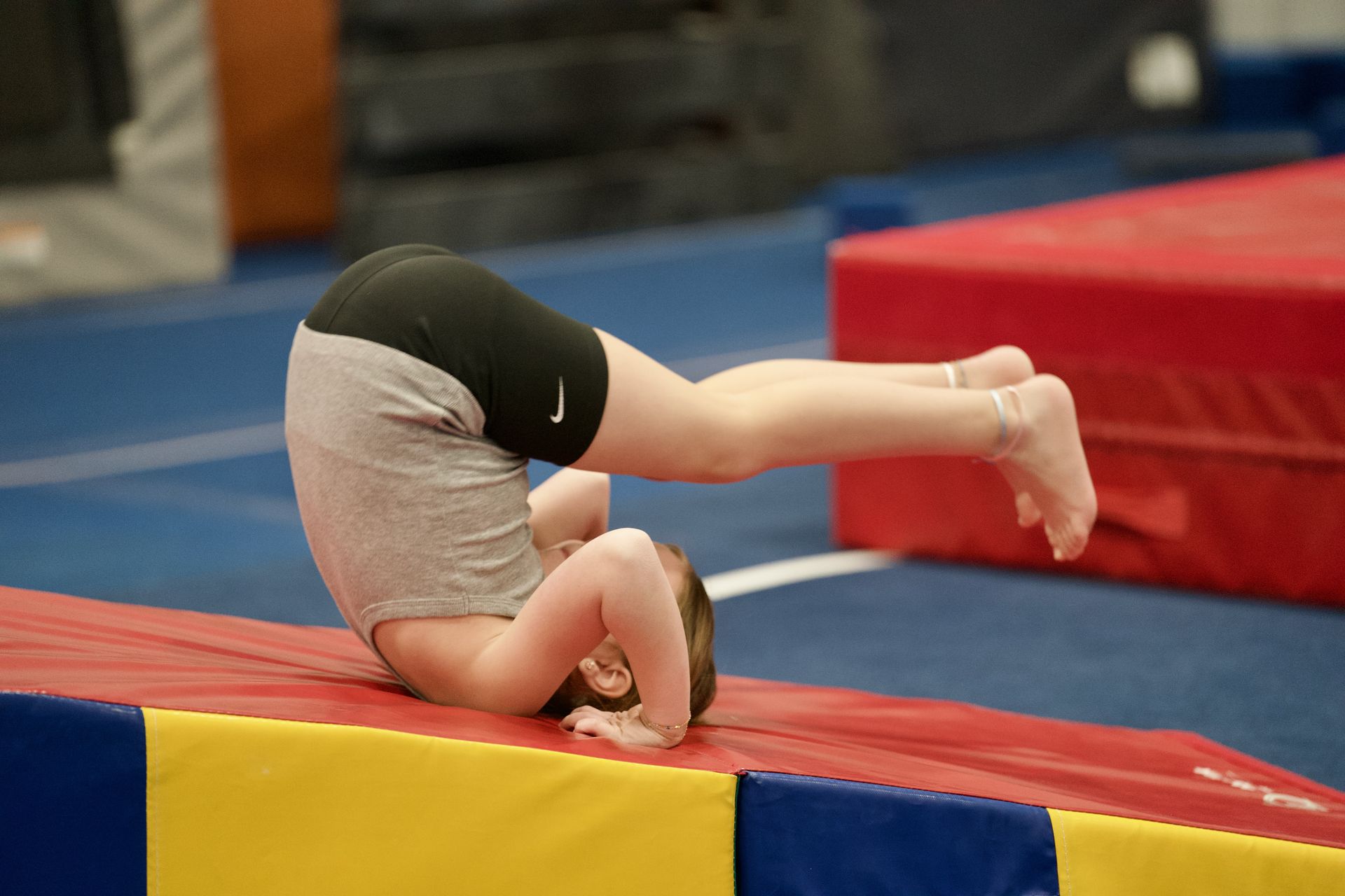 Gymnast doing a headstand on a red and yellow mat in a gym
