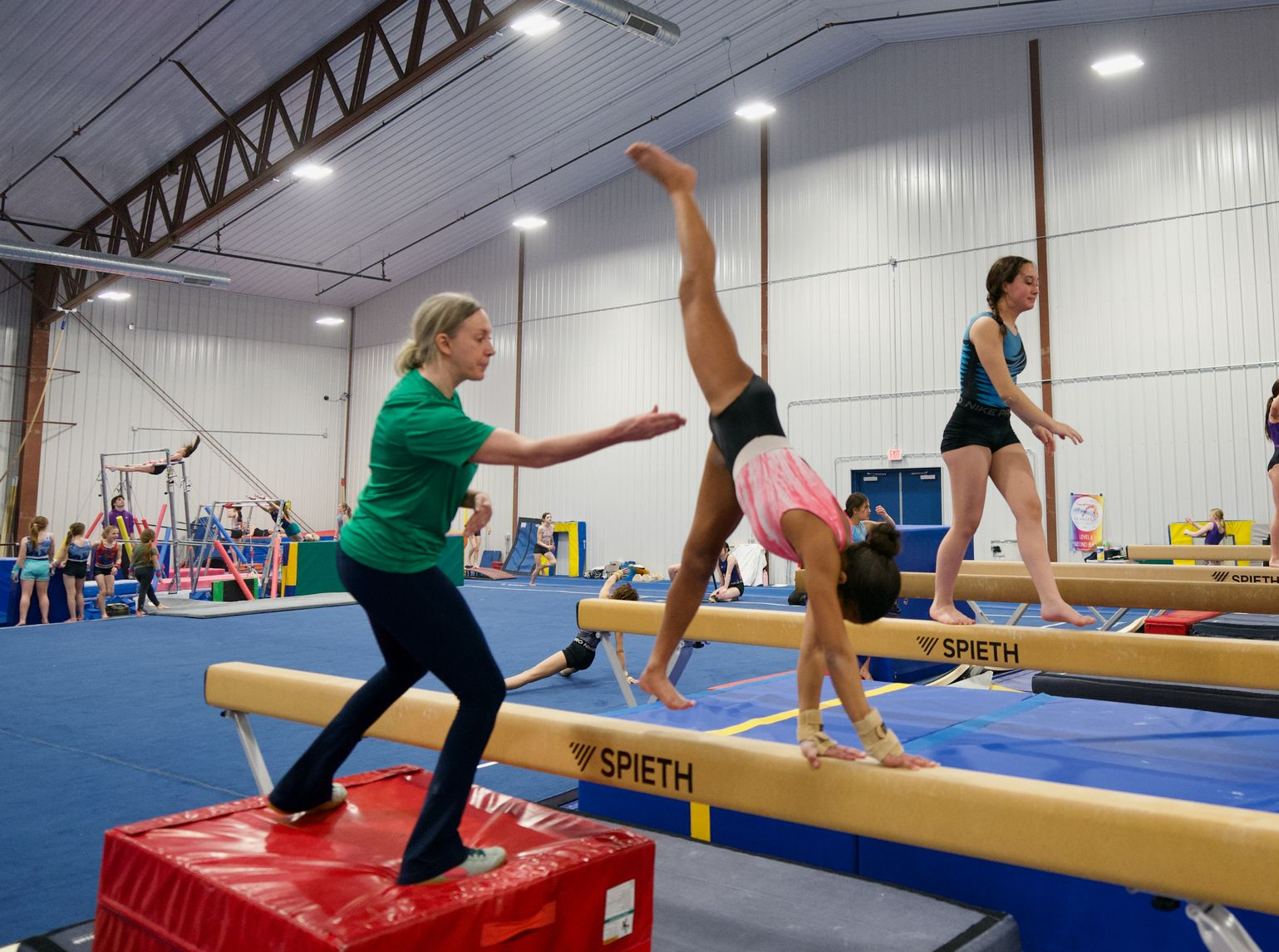 Cheer team posing in two rows on a blue mat against a beige gym wall.
