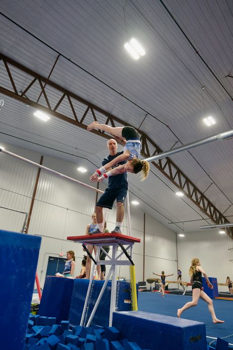 Two gymnasts balancing on a platform over mats in a gymnastics training gym