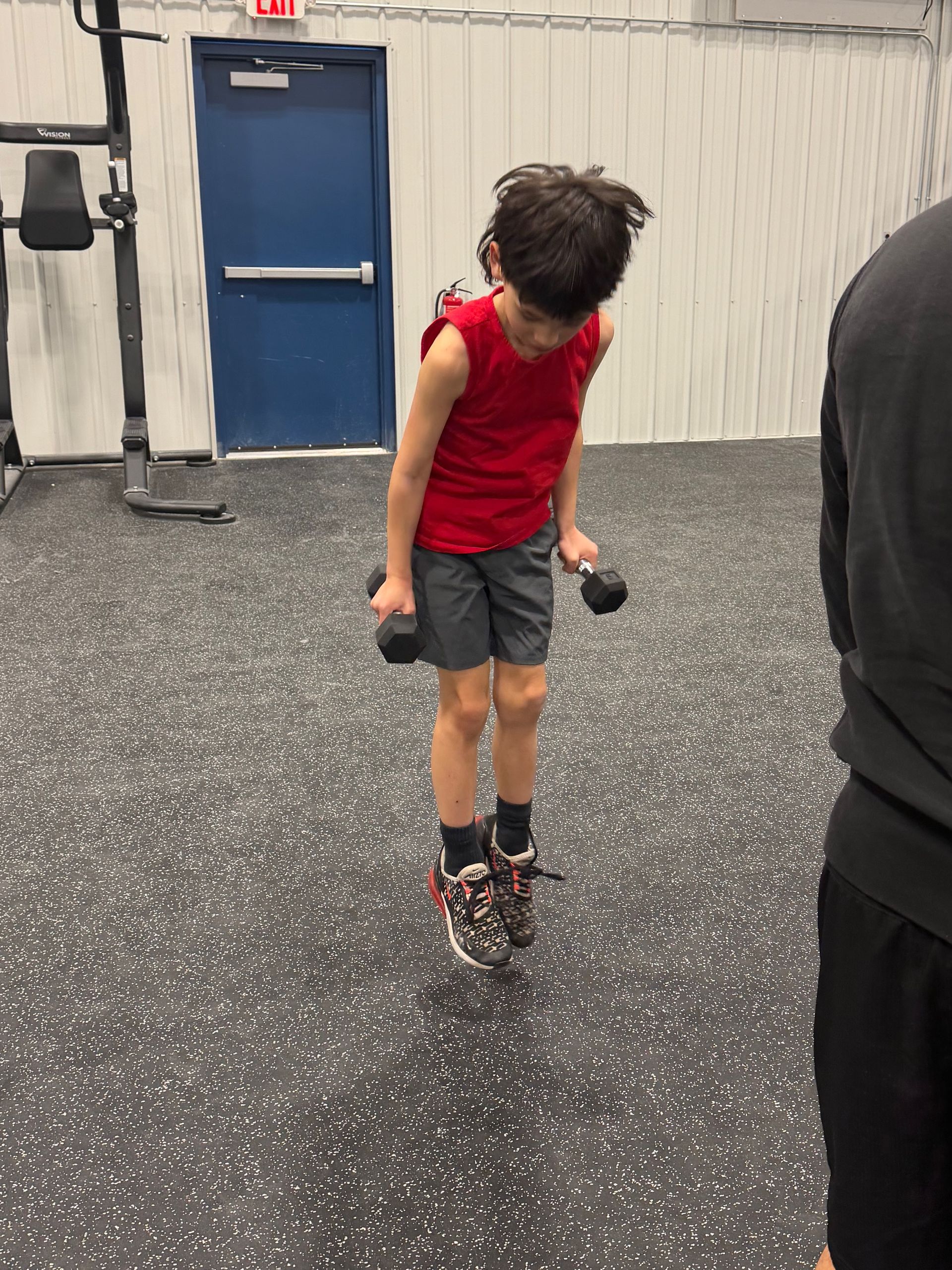 Child in a red shirt and black shorts jumps rope in a gym with a blue door in the background
