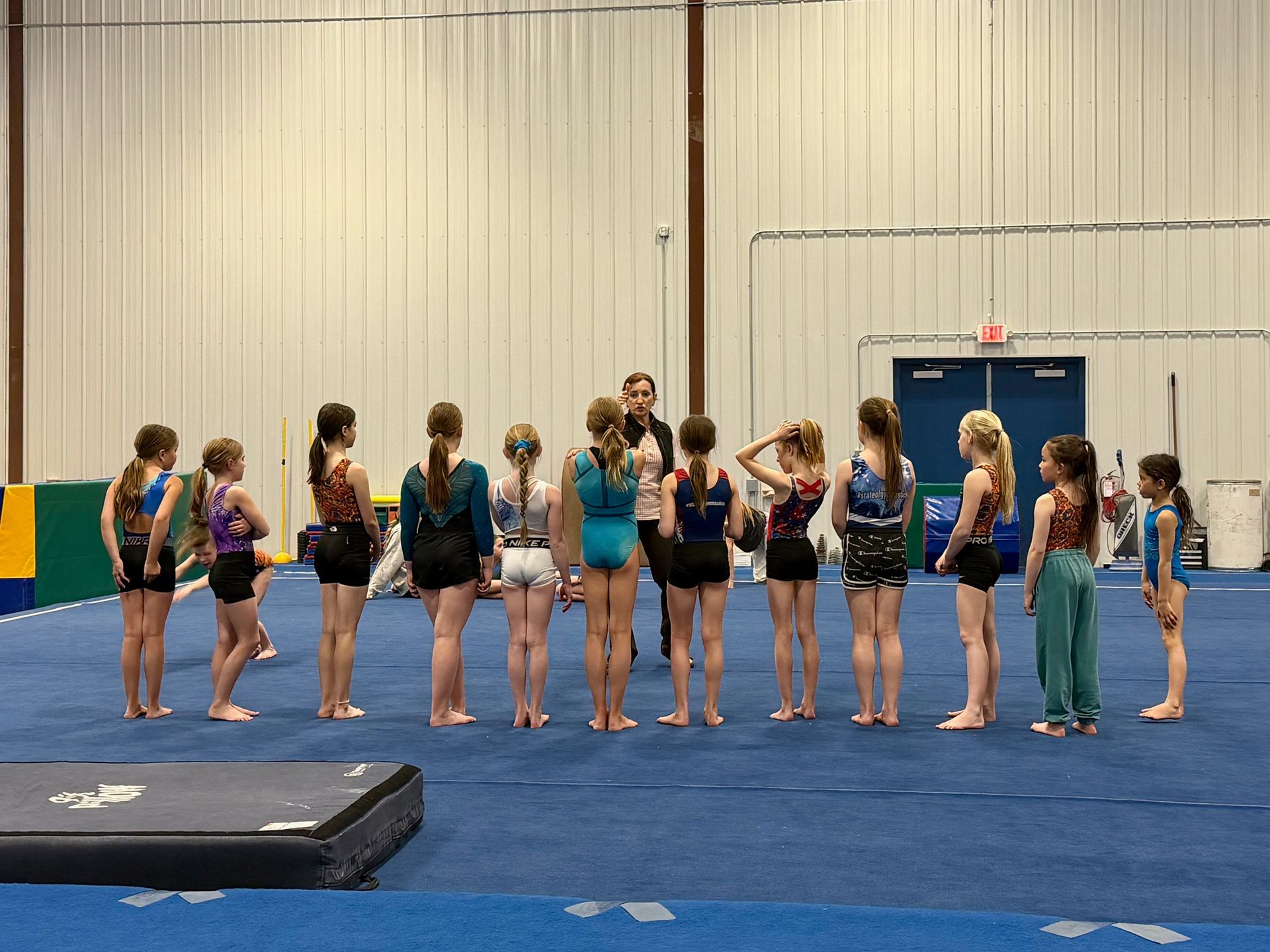 Gymnastics class standing in a line on a blue mat in an indoor gymnasium