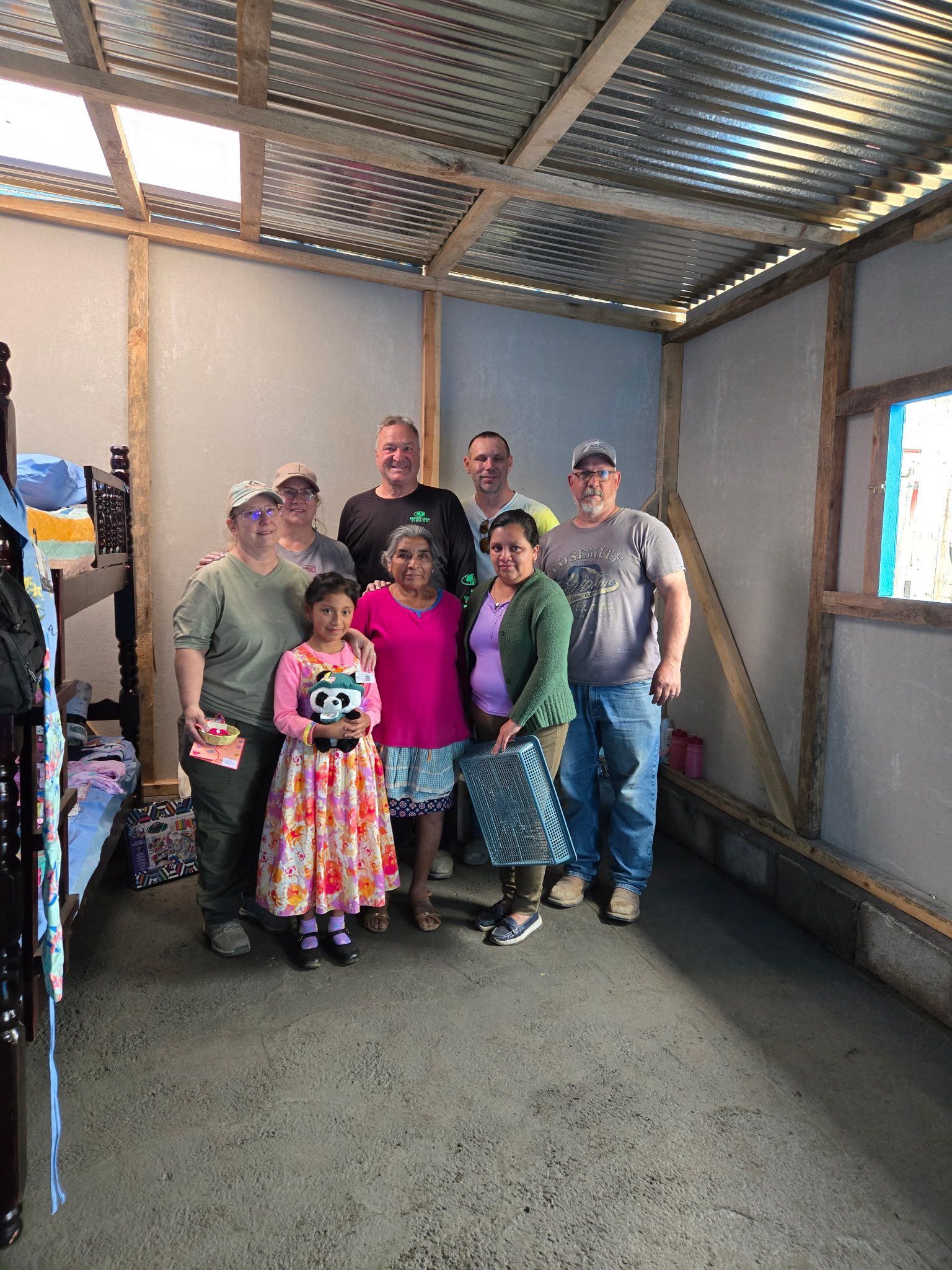 A group of people stand together inside a room with a corrugated metal ceiling and light-colored walls.