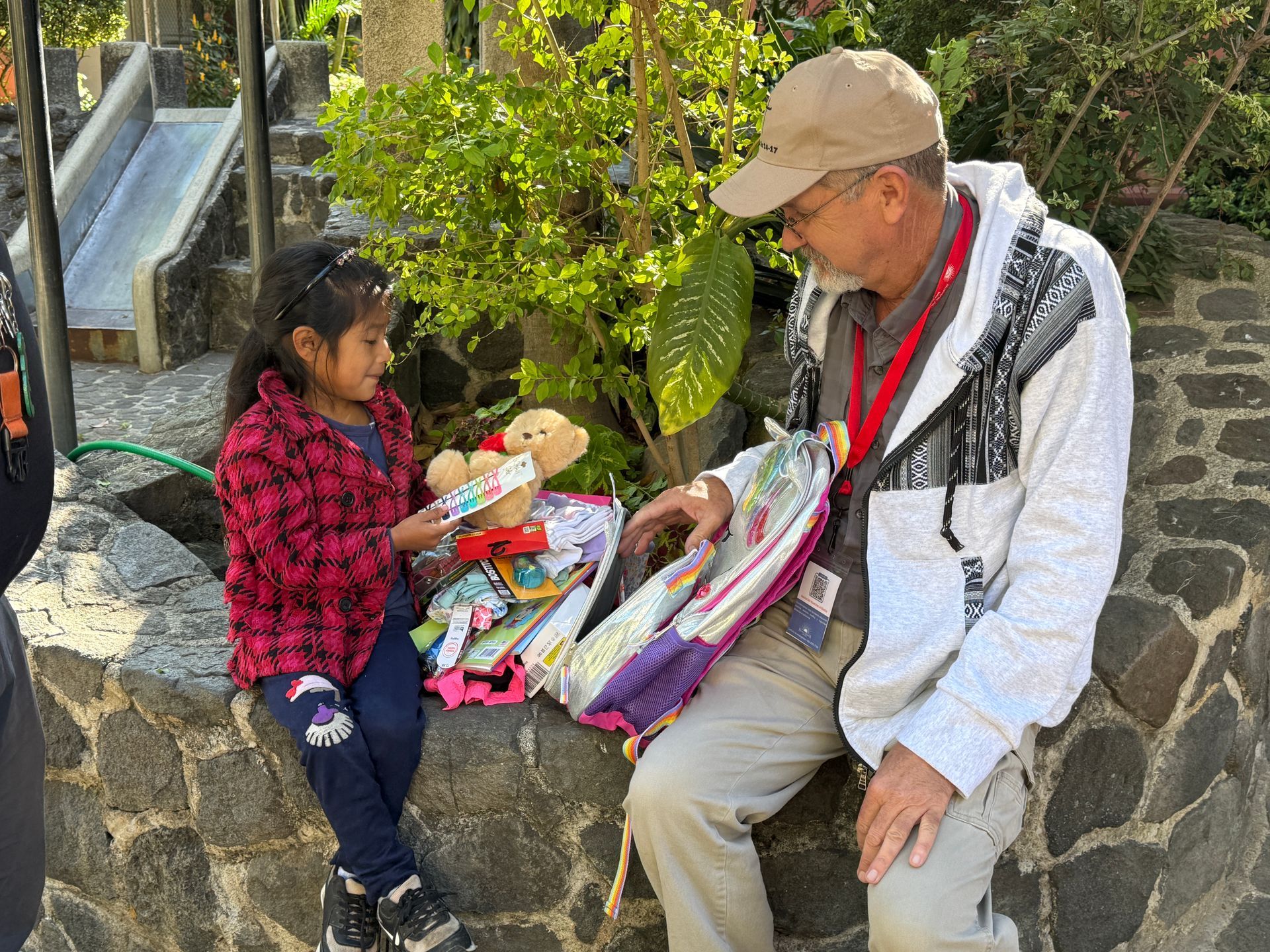 A man is sitting on a stone wall talking to a little girl.