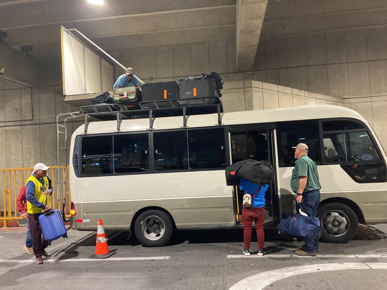 A group of people are loading luggage onto a bus in a parking lot.