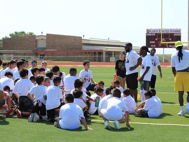 Youth football clinic on a field; coaches and kids in white shirts.