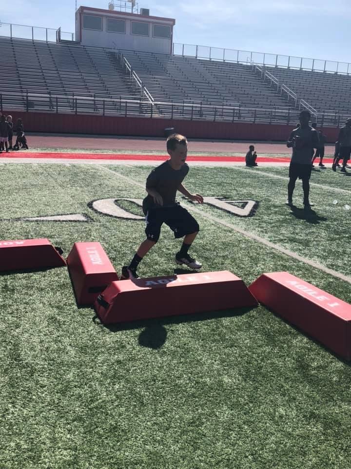 Boy on a football field doing agility drills, stepping over red padded blocks.