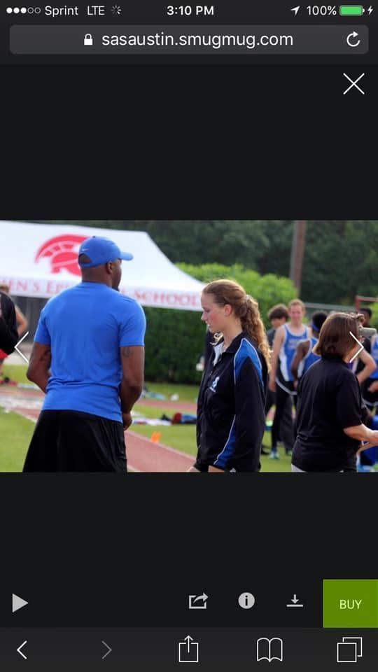 Coach in blue shirt talking to female athlete on track.