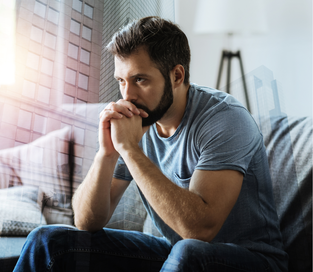 A man with a beard is sitting on a couch with his hands folded.
