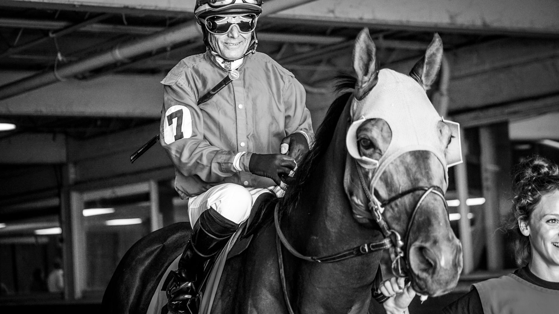 A black and white photo of a jockey riding a horse.