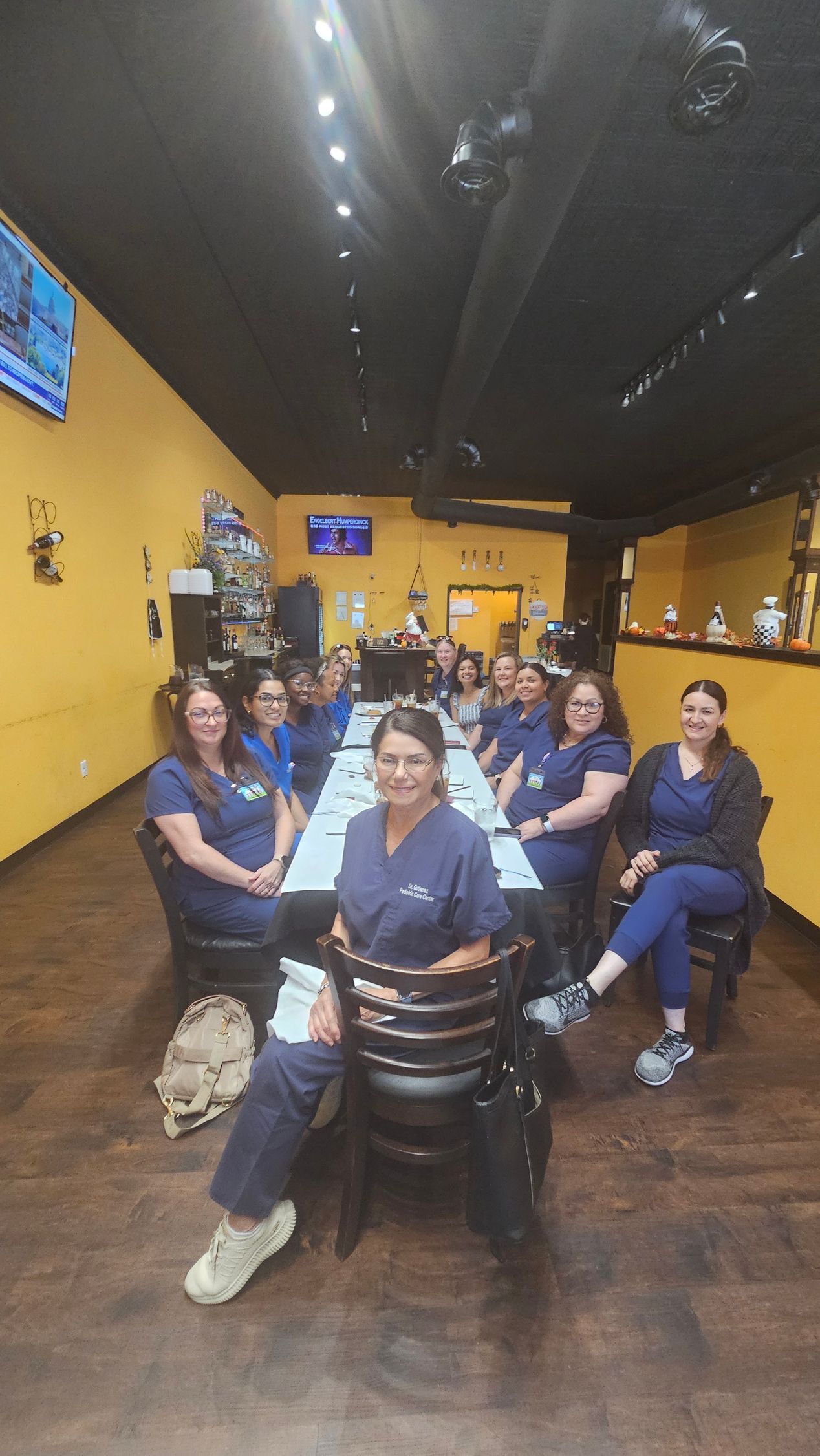 Group of people in blue scrubs seated around a long table in a restaurant.
