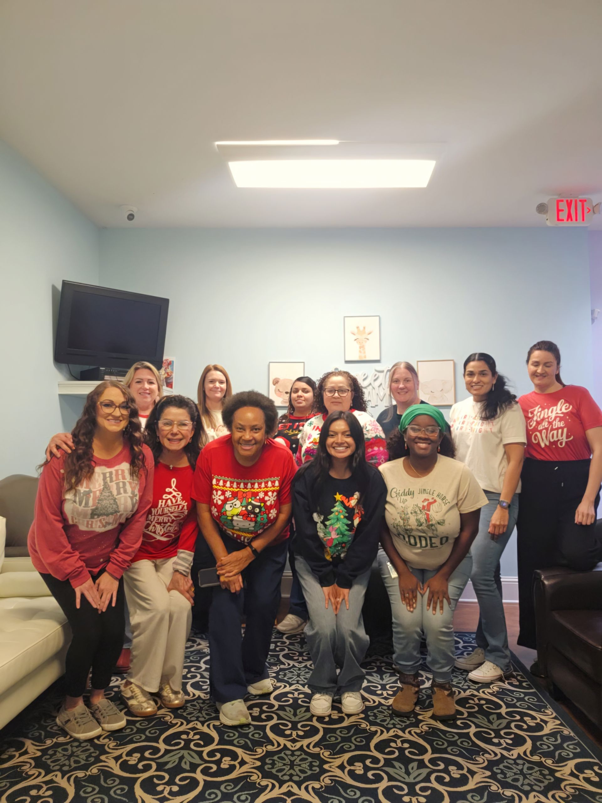Group of people wearing holiday sweaters, posing for a photo indoors.