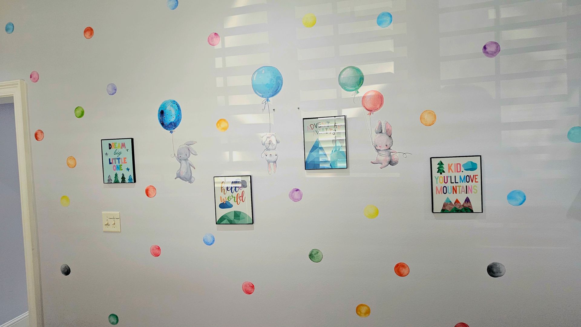 White wall decorated with colorful polka dots and framed artwork; window behind.