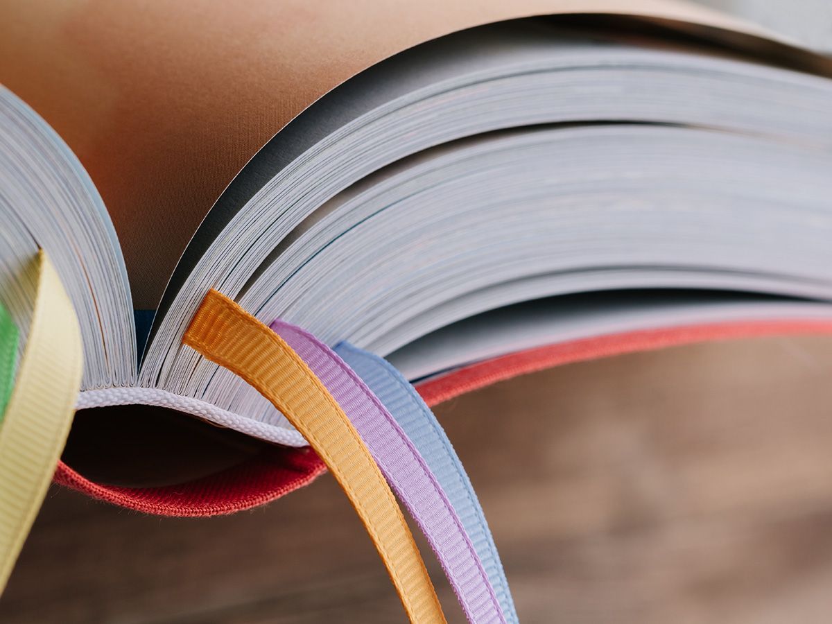 Close-up of an open book with colorful page edges and ribbon bookmarks against a blurred background