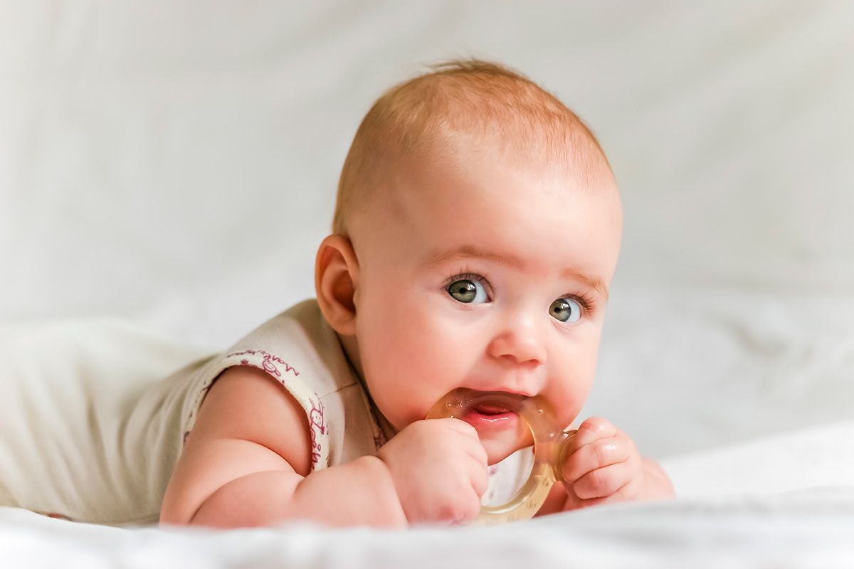 Baby lying on stomach, chewing a wooden teething ring.