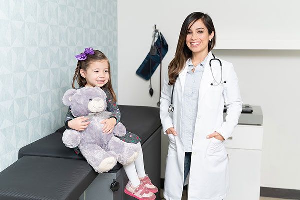 Smiling little girl with teddy bear in pediatric office